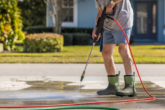 Man using pressure washer to power wash residential concrete driveway sidewalk.