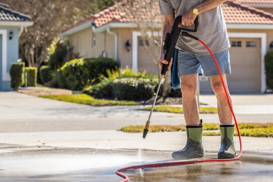 Man using pressure washer to power wash residential concrete driveway sidewalk.