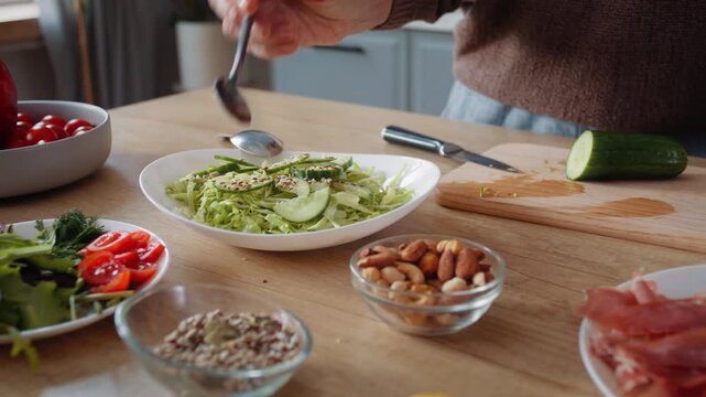 Old woman hand pours seeds onto salad on wooden counter closeup