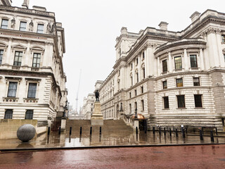 Naklejka premium London street scene with historic buildings statue and reflective wet pavement in central London