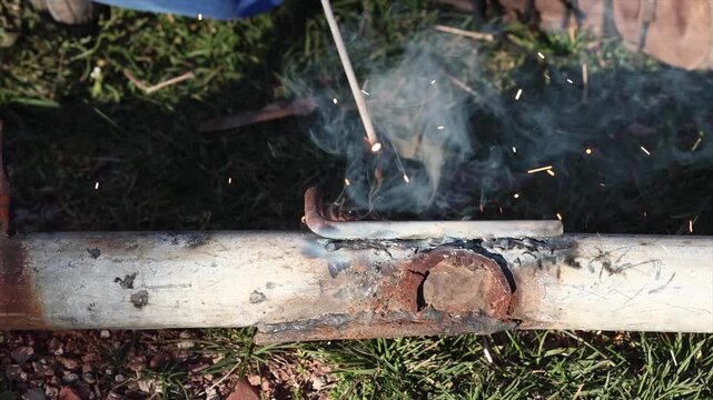 A welder is performing arc welding on an iron pipe in an open area.