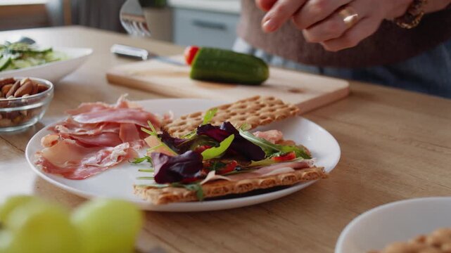Mature woman hand places prosciutto and salad onto crispbreads