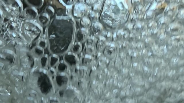 Close underwater view of numerous air bubbles in turbulent water filmed in slow motion with camera moving between submerged and surface.
