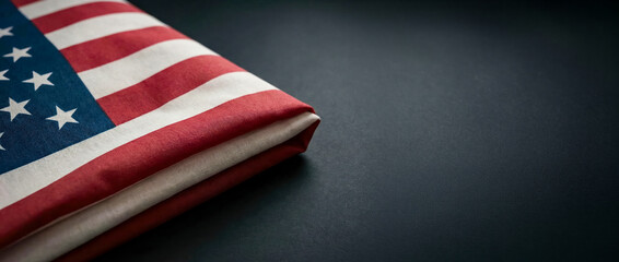 Obraz premium A folded American flag is placed on a black surface. The red and white stripes are clearly visible along with the blue field of stars. The focus is on the flag