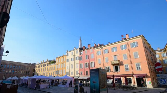 Modena, italy, april 11, 2026. Camera tilting up revealing the colorful historical buildings of piazza della pomposa in modena, italy, with a street market below