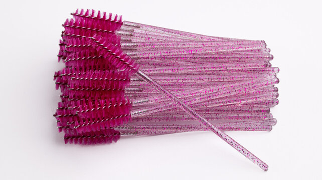 Close-up of pink glitter mascara wands and eyelash brushes on white background
