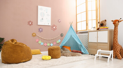 Colorful paper notes and beautiful decor hanging on beige wall near toy wigwam in stylish children's room with chest of drawers and poufs. Interior design © New Africa