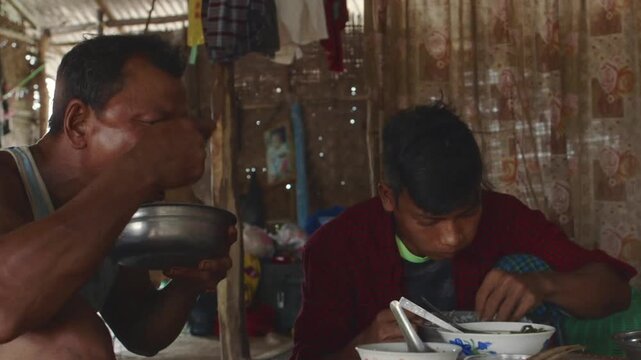 Two burmese men sharing a simple meal inside a humble bamboo hut in an oil field in Myanmar