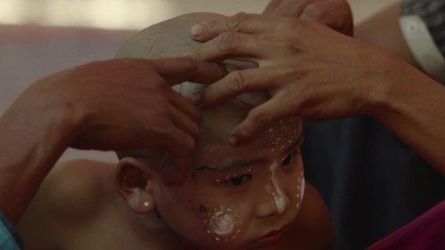Young Burmese boy participating in a traditional head shaving ceremony before becoming a novice monk
