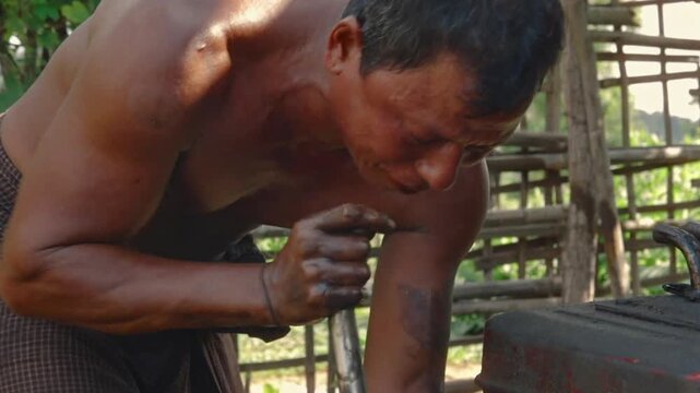 Asian man covered in crude oil performing hard manual labor at a makeshift extraction site