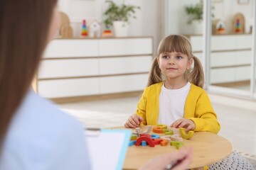 Professional psychologist working while little girl playing with toys at wooden table indoors, closeup