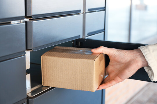Man taking out cardboard box from parcel locker outdoors, closeup