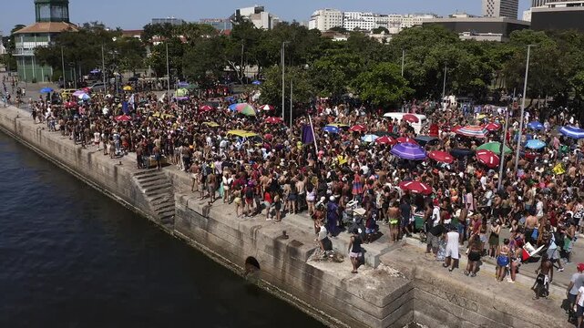 Drone Footage, Aerial view in traveling In mode passing by crowded people partying in Brazilian carnival of Rio de Janeiro with buildings and sugar loaf background in sunny day.