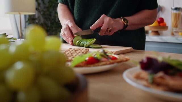 Hands of old woman cut cucumber with knife at countertop closeup