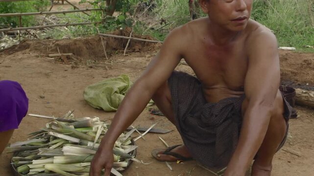 Middle aged Burmese worker crouching and chopping bamboo shoots in a village near an oil field in Myanmar