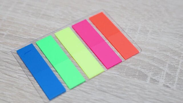Colorful sticky page markers arranged on wooden surface. Close-up stationery scene with office organization supplies.