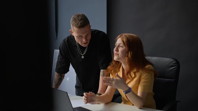Woman breaking into smile while chatting with young man, discussing plan of video record in studio