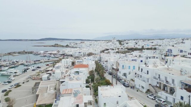 Aerial drone view of Naousa village on Paros island, Greece, showing traditional white buildings, coastal harbor and clear blue sea in daylight. Ideal for travel, tourism and Mediterranean lifestyle 
