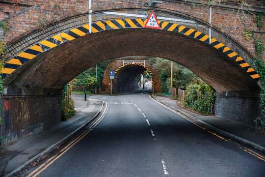 Empty Road Passing Under Brick Railway Bridge with Warning Markings