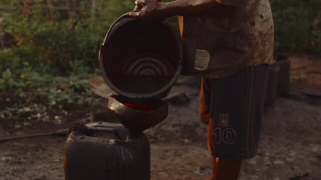 Burmese man working in unregulated oil field, pouring crude oil from a bucket into a jerrycan