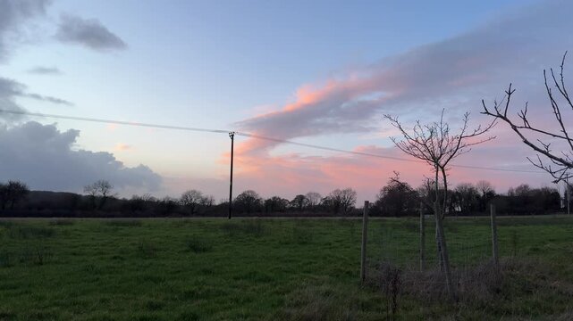 4K video of a beautiful pink sunset cloud formation over a green rural field and telegraph pole.