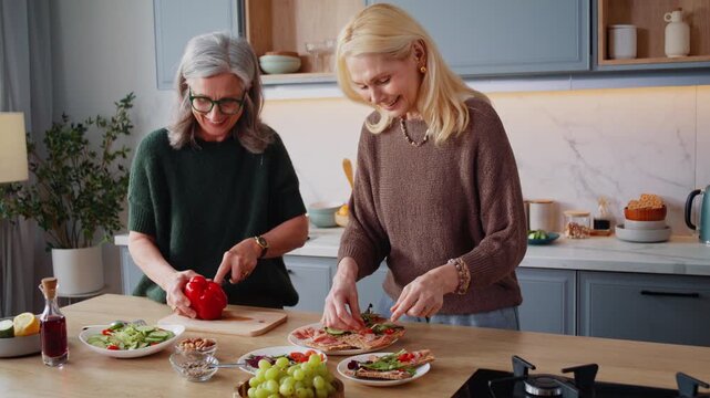 Old women friends cook lunch of sandwiches and salad in kitchen