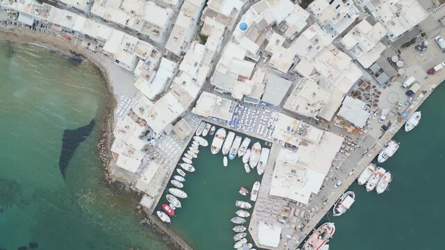Aerial drone view of Naousa village on Paros island, Greece, showing traditional white buildings, coastal harbor and clear blue sea in daylight. Ideal for travel, tourism and Mediterranean lifestyle 