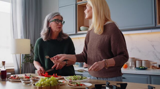 Happy senior women friends cook lunch and gossip in kitchen