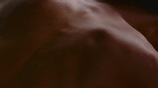 Detailed shot of a shirtless man's back muscles contracting and expanding while breathing heavily