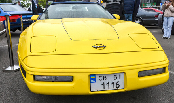 Yellow Chevrolet Corvette C4 with pop-up headlights and silver wheels parked at an outdoor event. A classic 80s American sports car icon