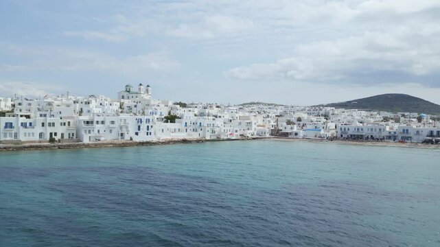 Aerial drone view of Naousa village on Paros island, Greece, showing traditional white buildings, coastal harbor and clear blue sea in daylight. Ideal for travel, tourism and Mediterranean lifestyle 