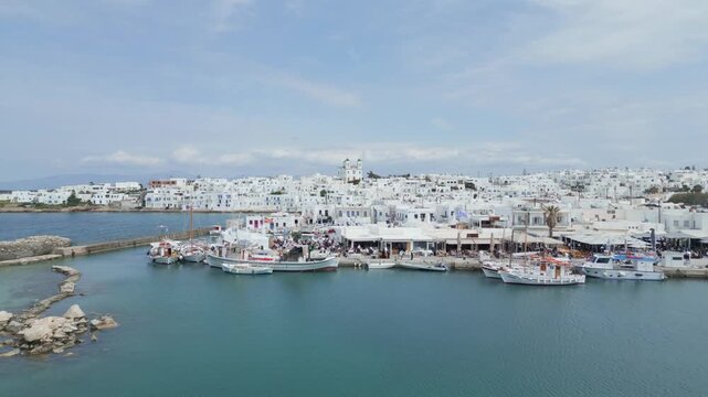 Aerial drone view of Naousa village on Paros island, Greece, showing traditional white buildings, coastal harbor and clear blue sea in daylight. Ideal for travel, tourism and Mediterranean lifestyle 