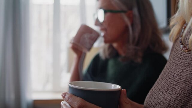Positive old women drink freshly brewed tea from cups in kitchen