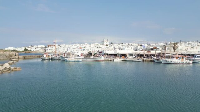 Aerial drone view of Naousa village on Paros island, Greece, showing traditional white buildings, coastal harbor and clear blue sea in daylight. Ideal for travel, tourism and Mediterranean lifestyle 