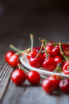 Close up of sweet cherries with green stems on rustic table. Fresh red summer fruit, shallow focus composition