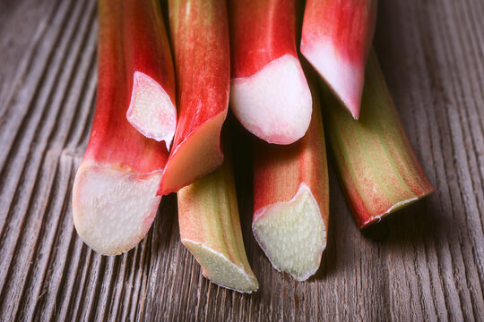 Close up of rhubarb stems on rustic wooden board, freshly cut edges. Natural organic rhubarb stalks detail, healthy cooking ingredient with vibrant tones