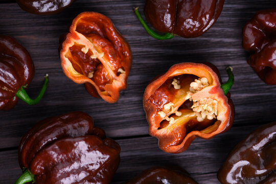 Chocolate habanero peppers with sliced halves showing seeds top view. Fresh chili pods natural food composition rustic surface