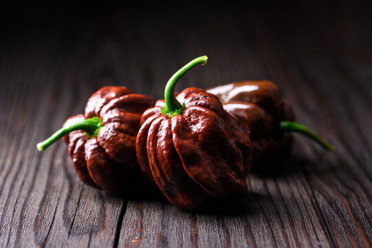 Chocolate habanero peppers arranged on rustic wooden table close view. Fresh chili pods with glossy surface natural food styling