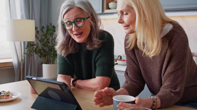Happy old women scroll internet on digital tablet in kitchen