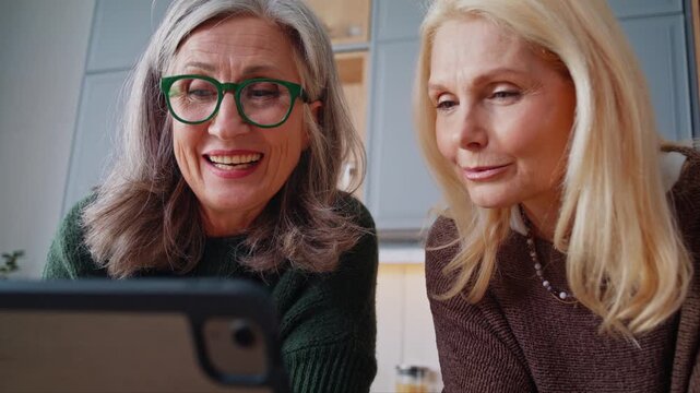 Smiling senior women watch video via digital tablet in kitchen