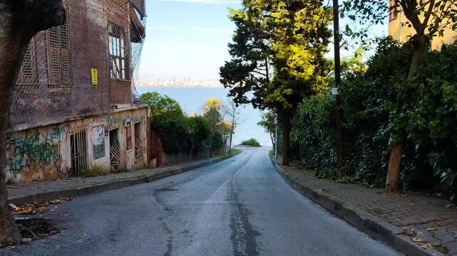 Picturesque Downhill Street in Kinaliada Island Featuring Historical Abandoned House, Graffiti Art, and Distant Istanbul Cityscape over the Marmara Sea in Autumn.