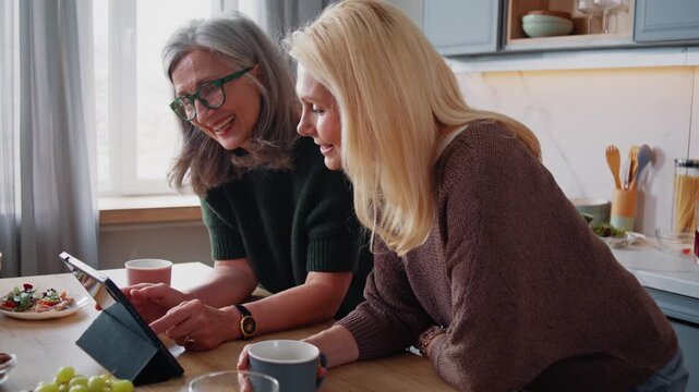 Happy old women watch online video via digital tablet in kitchen