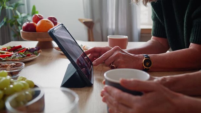 Senior women scroll social media feed on tablet at kitchen table