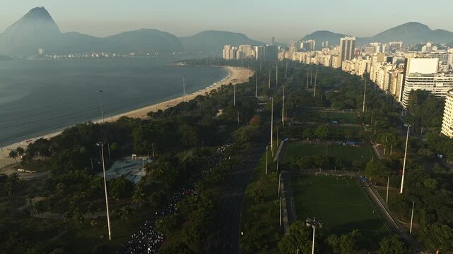 Drone Footage of many people running a race in highway of Flamengo Landfill (Aterro do Flamengo) passing by soccer fields with buildings in the right and sugar loaf background