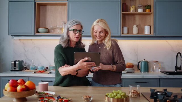 Happy mature women use tablet as discuss content in kitchen