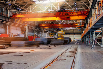 Stack of steel sheets and gantry crane in metalworking factory warehouse