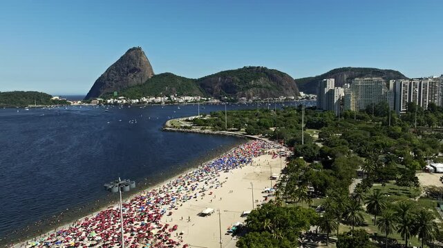 Aerial View, Drone Footage of Aterro do Flamengo traveling out by trees and vegetation of Flamengo landfill, the beach with sugar loaf mountain and boats in the sea background in a summer day