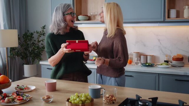 Mature woman presents surprise gift to best friend in kitchen