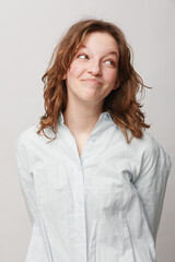 Obraz premium Young woman with curly hair wearing white shirt looks sideways with playful smile. Studio portrait on light background. Concept of casual style, happiness, and natural expression.