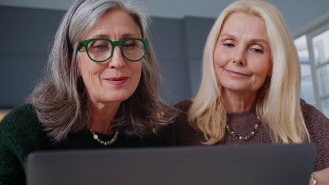 Mature women watch laptop together following online content
